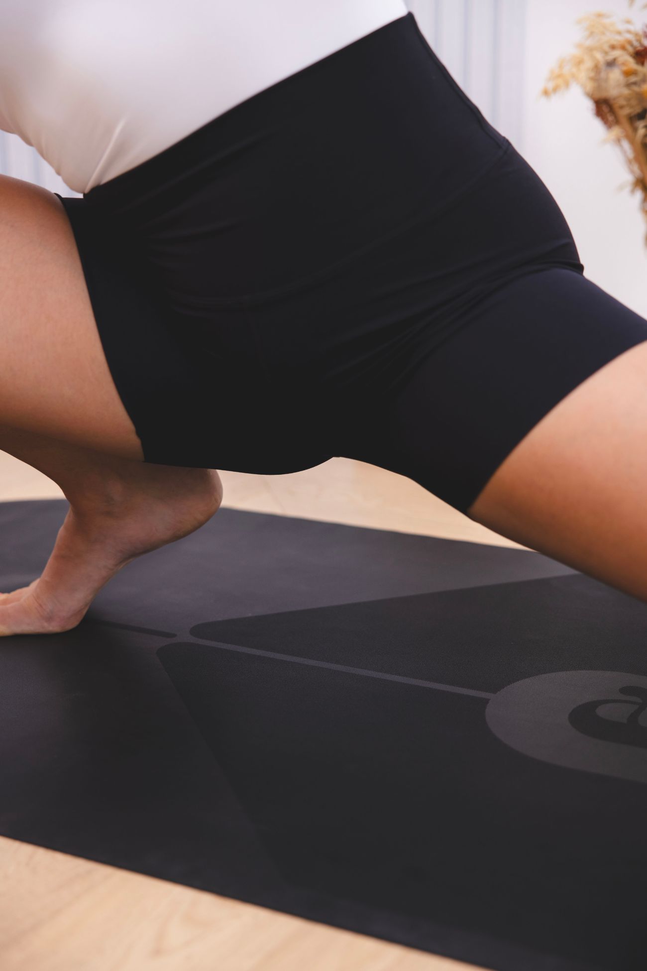 Posture Skandasana sur tapis de yoga Ogma Travel noir – souplesse et équilibre Posture Skandasana sur le tapis de voyage Ogma noir Oshun, format compact, antidérapant et au design ovale à double arrondi.